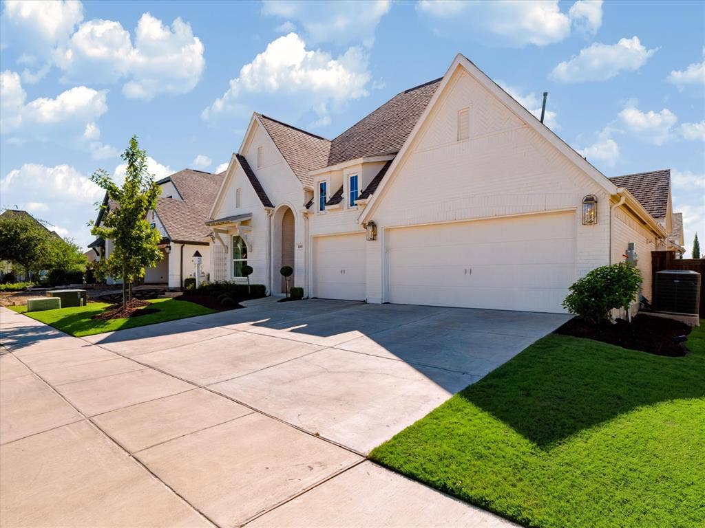 1103 Sandgate Drive, Forney, TX 75126 Light-colored brick exterior featuring a multi-gabled roofline, three-car garage, and concrete driveway