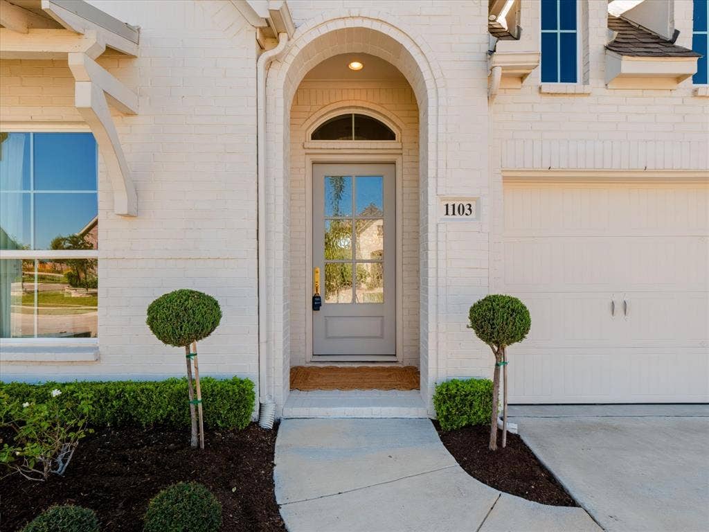 1103 Sandgate Drive, Forney, TX 75126 Painted brick exterior with an arched entryway, transom window, six-pane glass front door, and concrete walkway