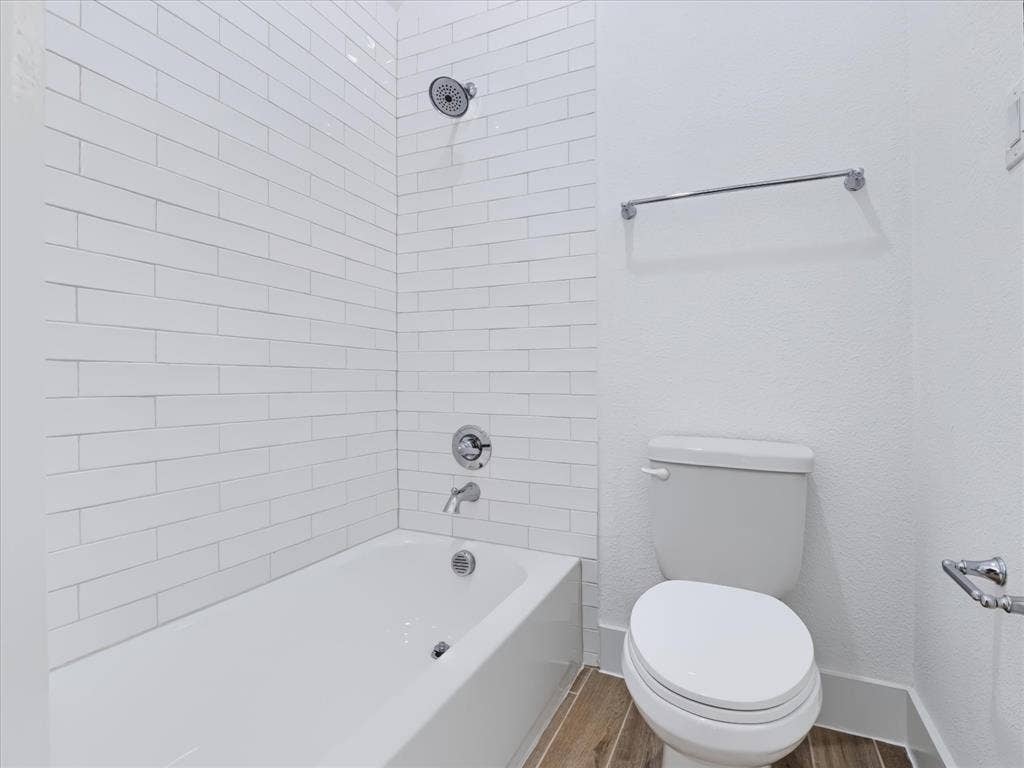 1103 Sandgate Drive, Forney, TX 75126 Full-height white subway tile surround, integrated bathtub with polished chrome fixtures, elongated toilet, and wood-finish flooring
