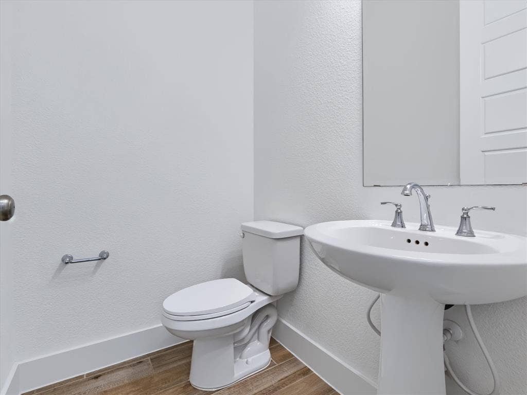 1103 Sandgate Drive, Forney, TX 75126 Pedestal sink with a widespread chrome faucet, wall-mounted mirror, white ceramic toilet, and wood-finish flooring