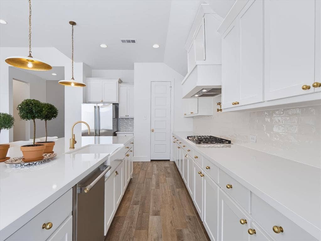 1103 Sandgate Drive, Forney, TX 75126 Kitchen featuring white cabinetry, solid surface countertops, a farmhouse-style apron sink, brass-finish hardware, and wood-finish flooring
