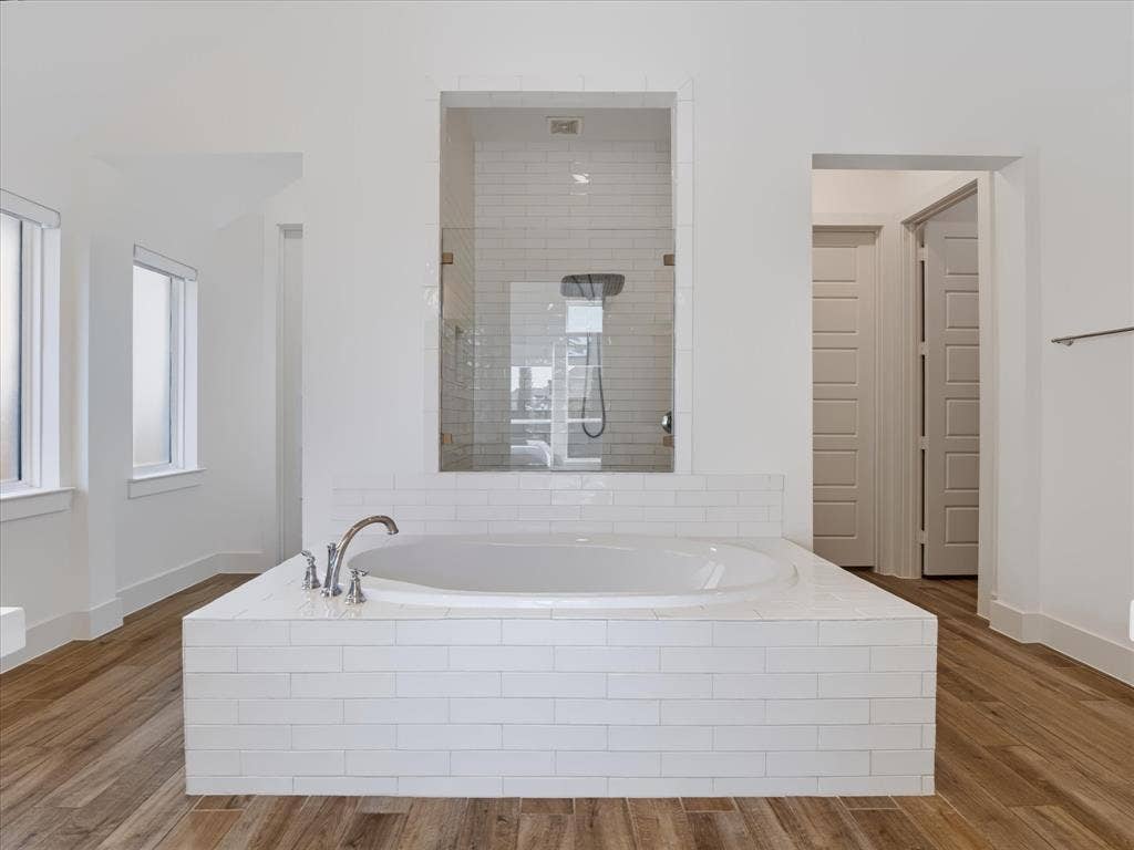 1103 Sandgate Drive, Forney, TX 75126 Built-in soaking tub with white subway tile surround, wood-finish flooring, glass-enclosed shower, and polished chrome fixtures