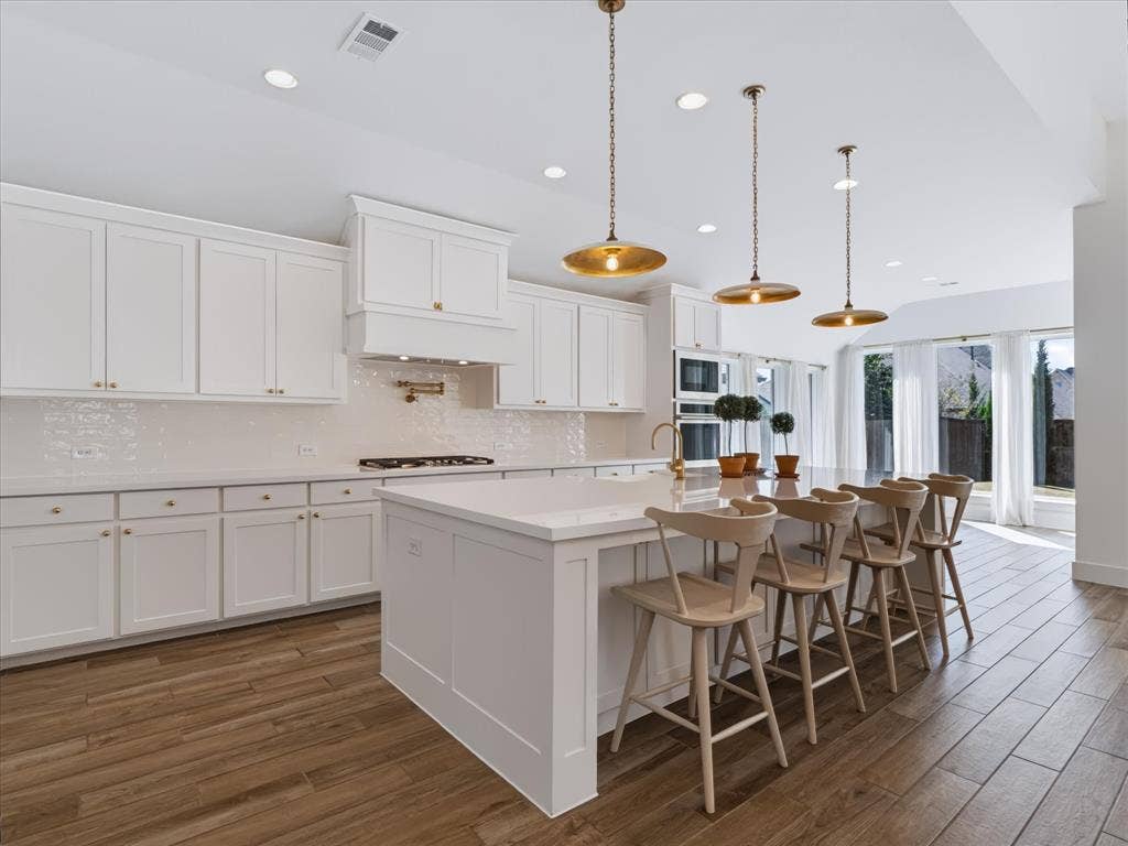 1103 Sandgate Drive, Forney, TX 75126 Kitchen featuring white shaker-style cabinetry, a quartz-topped center island with seating, built-in double wall ovens, wood-finish flooring, and metallic pendant lighting
