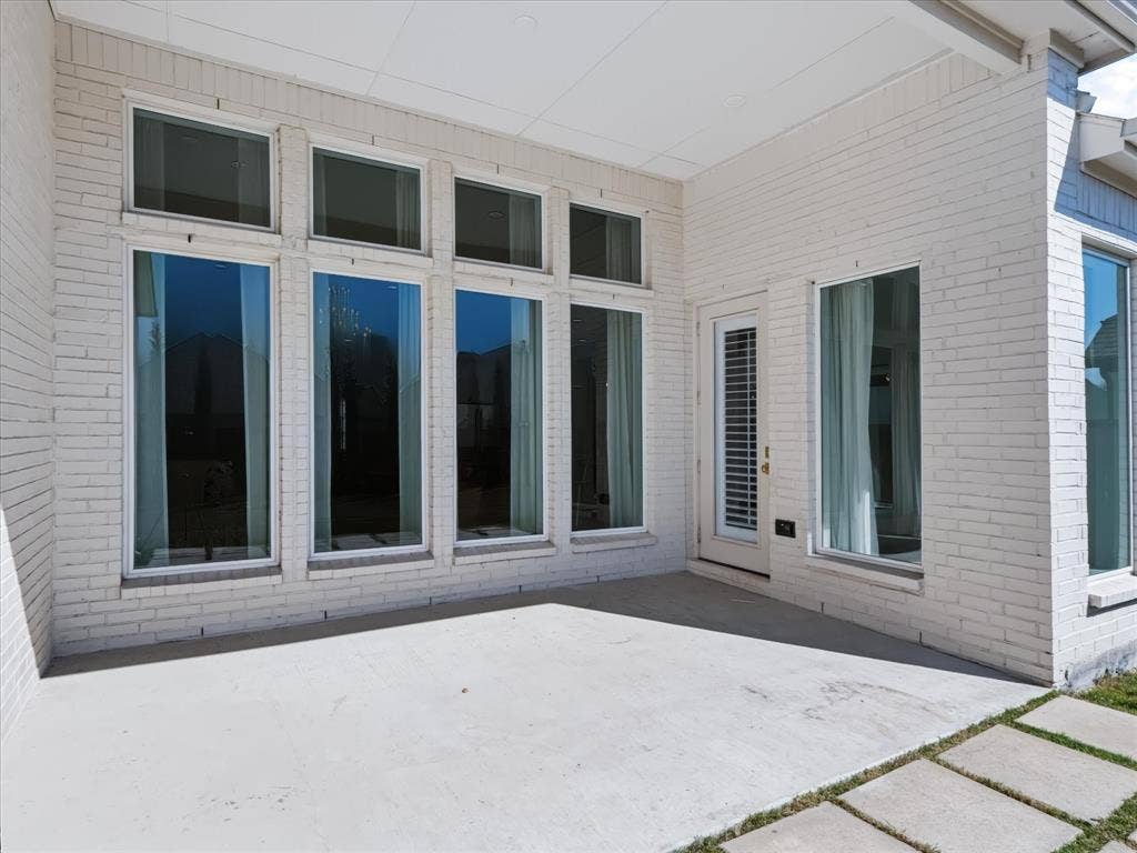 1103 Sandgate Drive, Forney, TX 75126 Covered patio featuring white brick exterior walls, concrete flooring, large floor-to-ceiling windows, and glass-paneled exterior door
