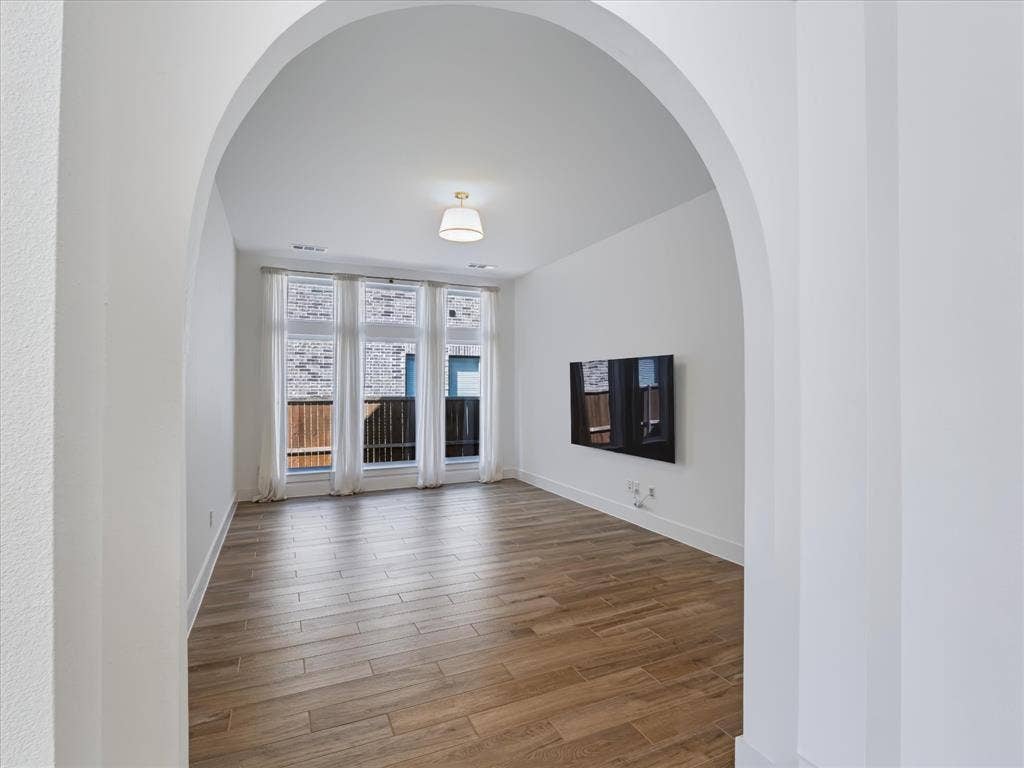 1103 Sandgate Drive, Forney, TX 75126 Interior space featuring an architectural arched entryway, wood-finish flooring, a wall-mounted light fixture, and floor-to-ceiling windows