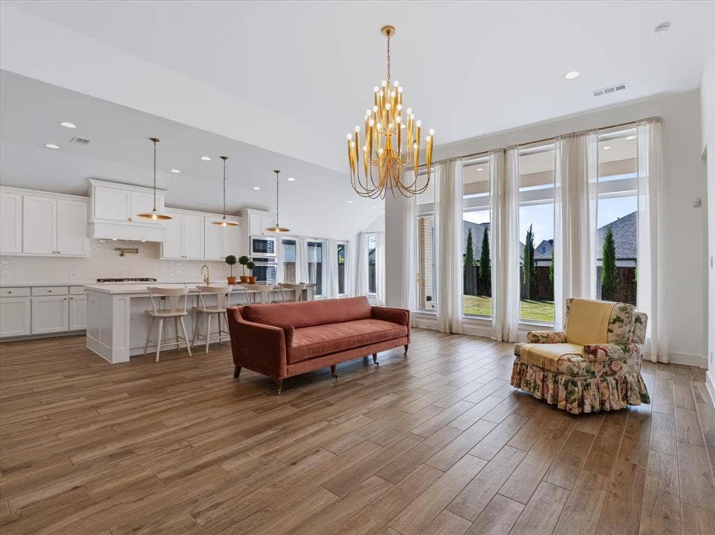 1103 Sandgate Drive, Forney, TX 75126 Open-concept interior featuring wood-finish flooring, a kitchen with white cabinetry and a central island, recessed lighting, and a gold-finish tiered chandelier