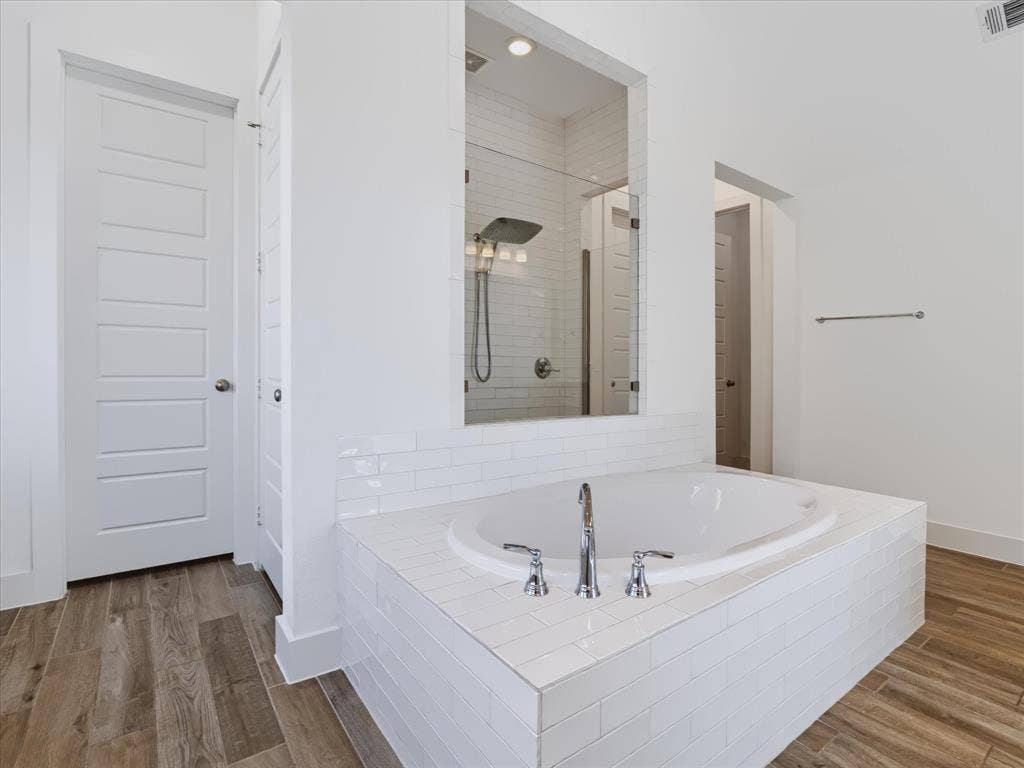 1103 Sandgate Drive, Forney, TX 75126 Oval soaking tub with polished chrome fixtures, white subway tile surround, recessed glass-enclosed shower, and wood-finish flooring