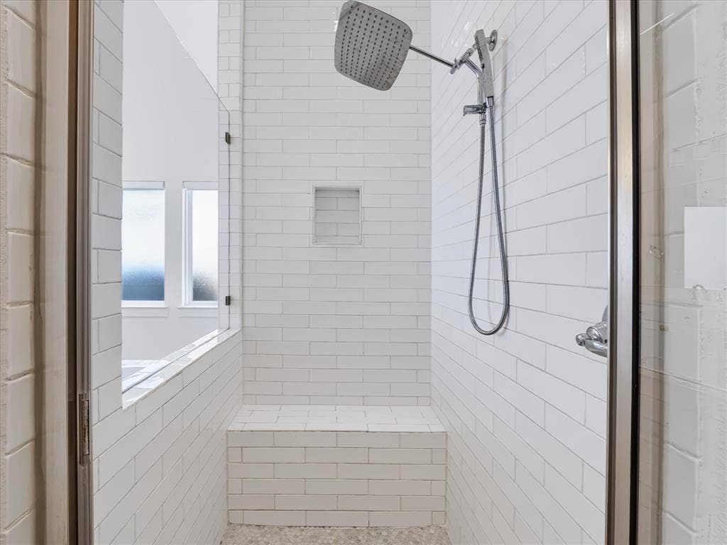1103 Sandgate Drive, Forney, TX 75126 Walk-in shower featuring white subway tile walls, a built-in bench, a recessed wall niche, a square rainfall showerhead, and a hand-held sprayer