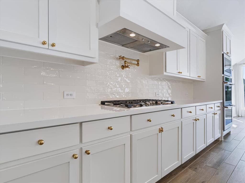 1103 Sandgate Drive, Forney, TX 75126 Kitchen featuring white shaker-style cabinetry, a glossy subway tile backsplash, solid-surface countertops, gold-tone hardware, and a wall-mounted pot filler