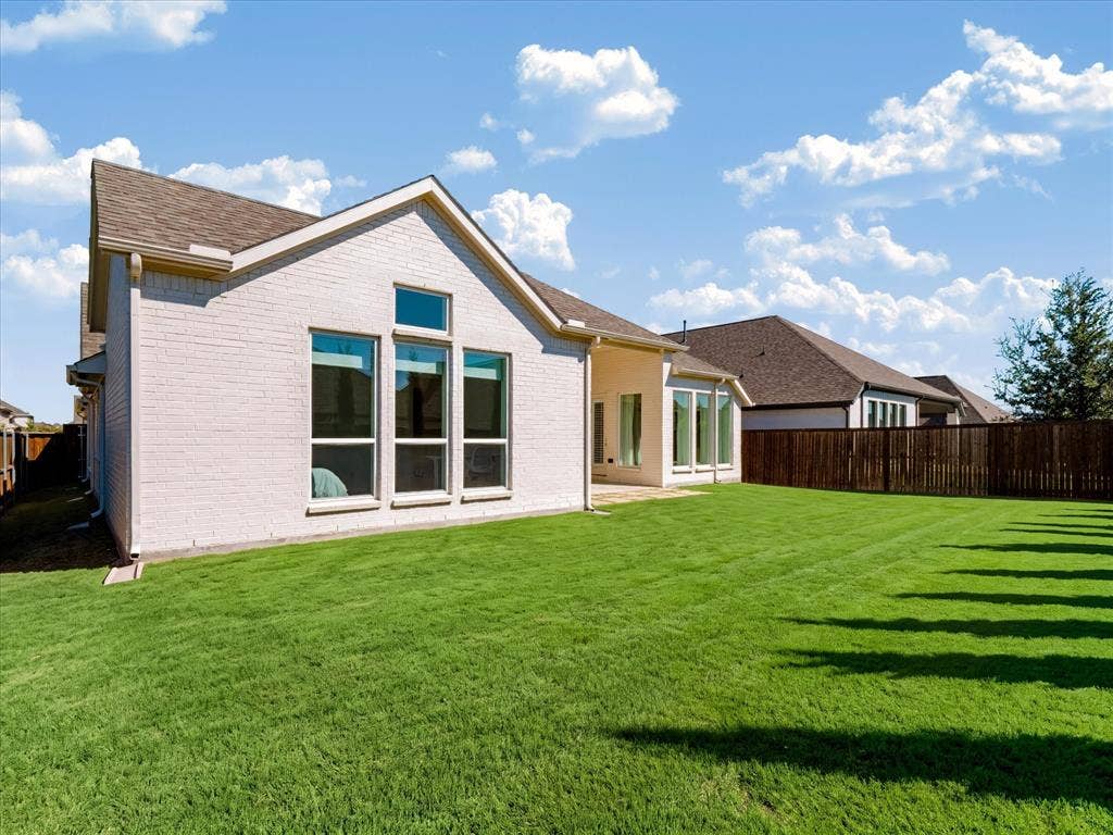 1103 Sandgate Drive, Forney, TX 75126 Light-colored brick exterior featuring oversized windows, a pitched shingle roof, and a fenced backyard with a lawn