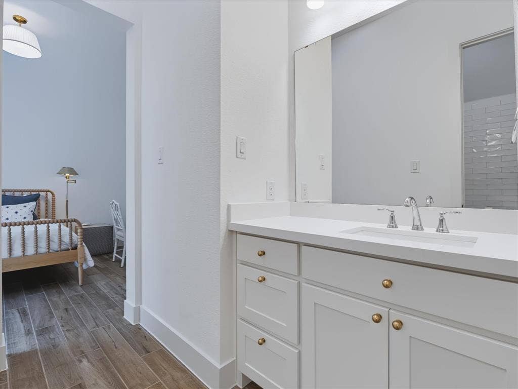 1103 Sandgate Drive, Forney, TX 75126 Bathroom vanity featuring white cabinetry, a solid-surface countertop, an integrated rectangular sink, brass-finish hardware, and a large-format vanity mirror