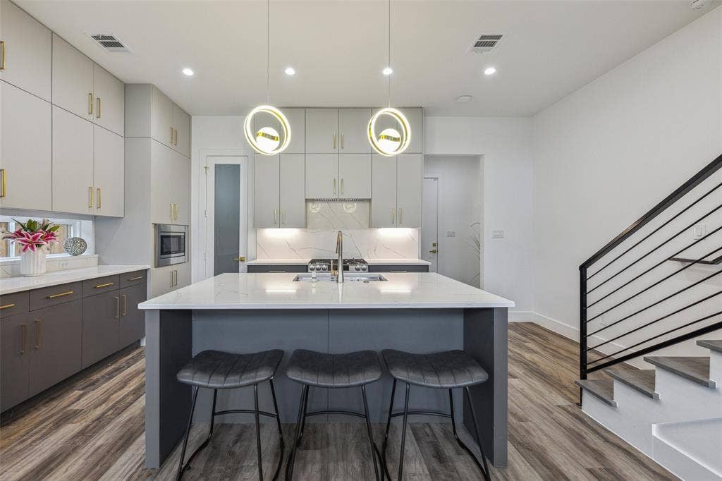 Kitchen featuring backsplash, hanging light fixtures, stainless steel microwave, hardwood / wood-style flooring, and a center island with sink