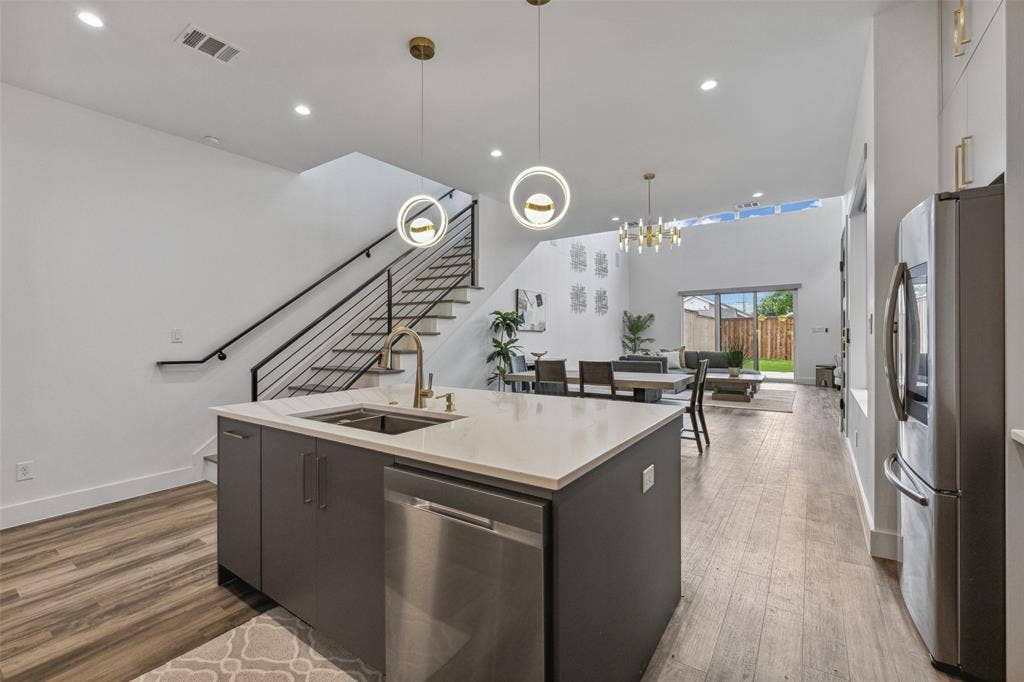 Kitchen featuring appliances with stainless steel finishes, decorative light fixtures, sink, a center island with sink, and hardwood / wood-style flooring