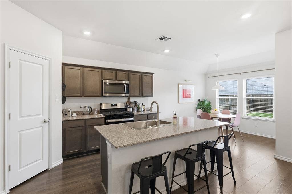1108 Emerald Gate Drive, Princeton, TX 75407 Kitchen featuring dark-toned cabinetry, a spacious island with stone-finish countertops, stainless steel appliances, wood-finish flooring, and recessed lighting