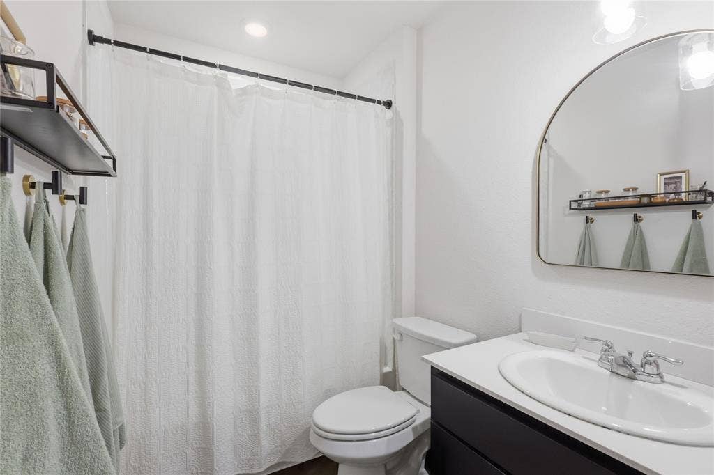 1108 Emerald Gate Drive, Princeton, TX 75407 Bathroom featuring a vanity with a white countertop and oval under-mount sink, an arched wall-mounted mirror, matte black hardware, and a built-in wall shelf