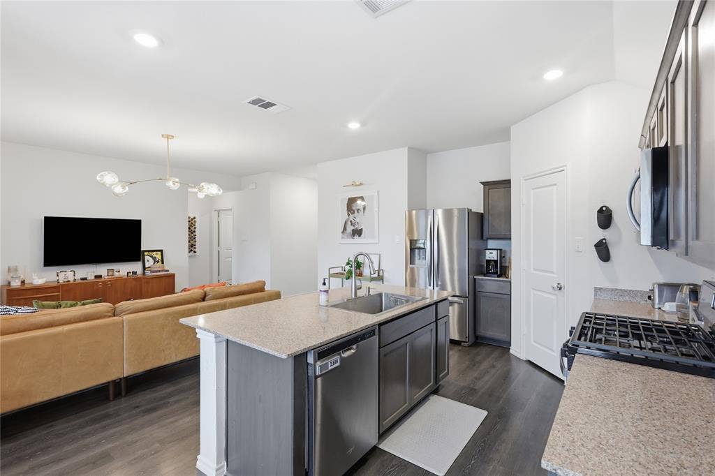 1108 Emerald Gate Drive, Princeton, TX 75407 Kitchen featuring a central island with stone-surface countertops, dark wood cabinetry, recessed lighting, and stainless steel appliances, complemented by wood-finish flooring