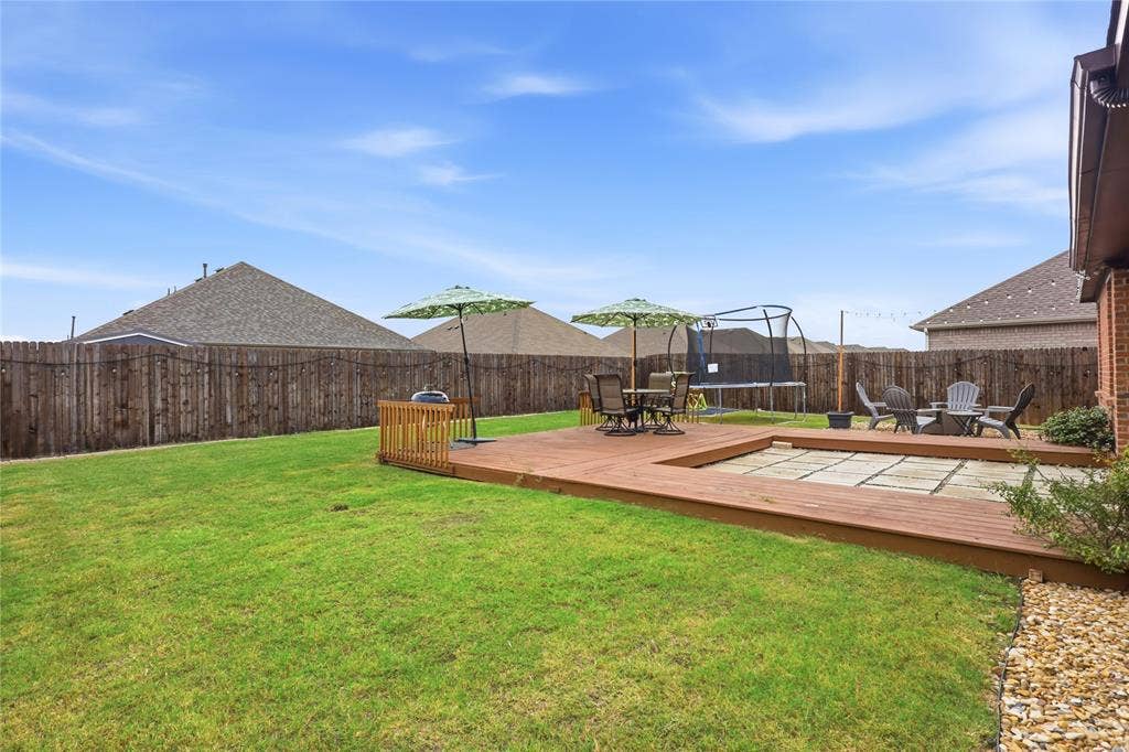 1108 Emerald Gate Drive, Princeton, TX 75407 Rear yard featuring a wood deck with an integrated stone paver patio, a perimeter wood privacy fence, and an expansive lawn
