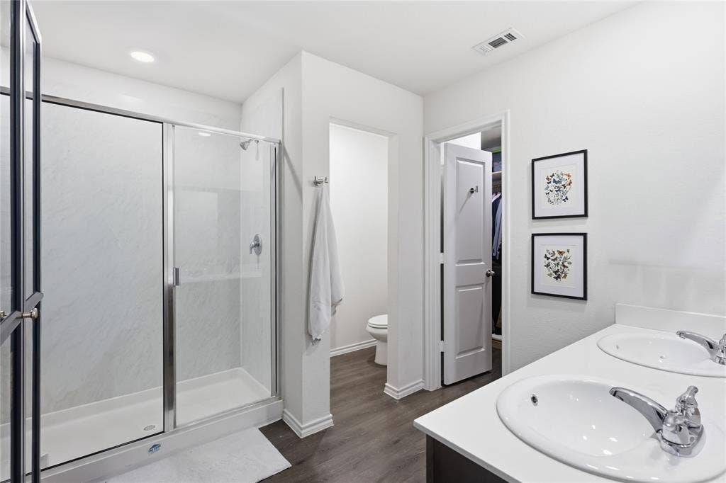 1108 Emerald Gate Drive, Princeton, TX 75407 Bathroom featuring a dual-sink vanity with a solid-surface countertop, walk-in shower with a glass enclosure, wood-finish flooring, and recessed lighting