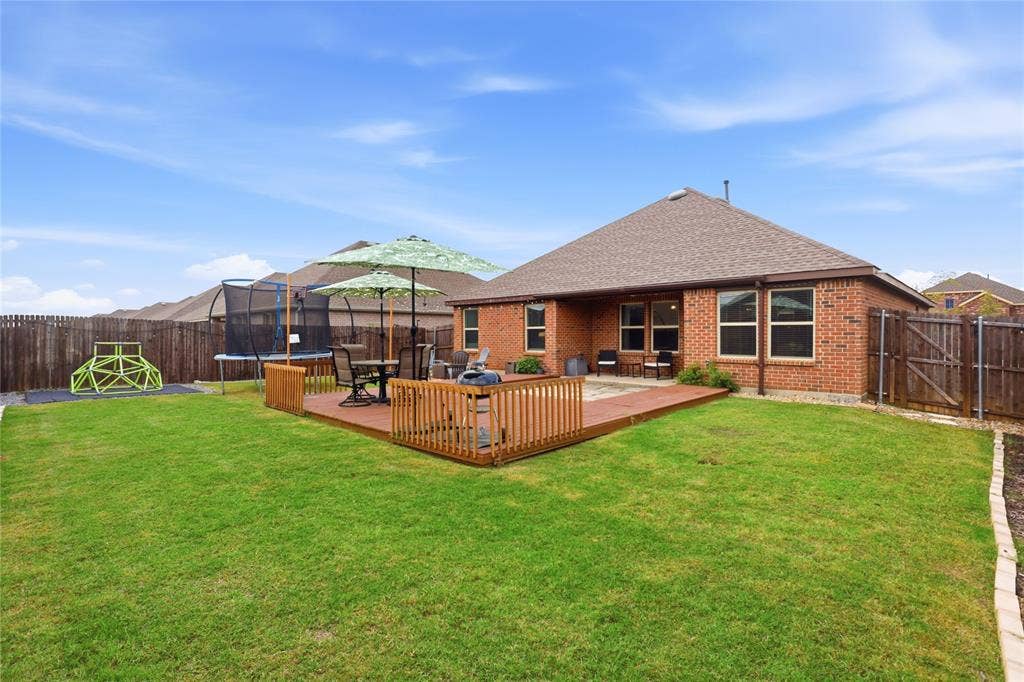 1108 Emerald Gate Drive, Princeton, TX 75407 Spacious backyard featuring a brick exterior, a raised wood deck with railing, and perimeter wood privacy fencing