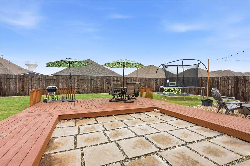 1108 Emerald Gate Drive, Princeton, TX 75407 Backyard featuring a raised wood-finish deck, a rectangular stone paver patio area, and a wood privacy fence