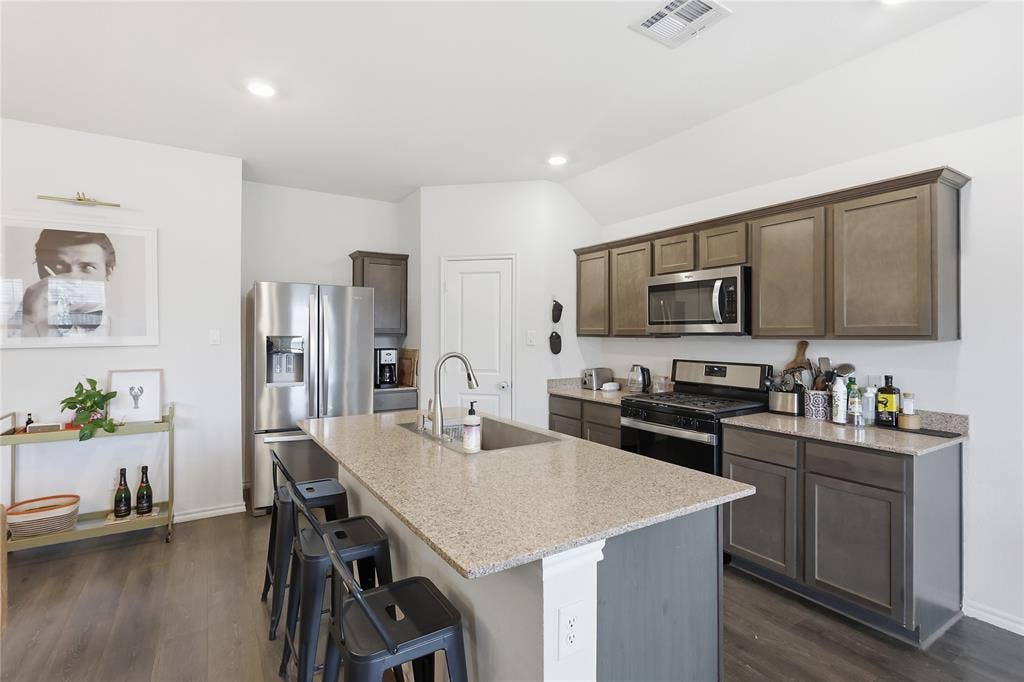1108 Emerald Gate Drive, Princeton, TX 75407 Kitchen featuring shaker-style cabinetry, stone-surface countertops, a center island with an undermount sink, stainless steel appliances, and wood-finish flooring