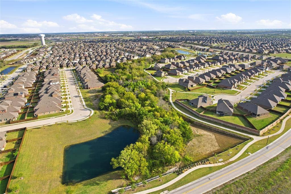 1108 Emerald Gate Drive, Princeton, TX 75407 Aerial perspective of a master-planned community featuring a central pond, established tree canopy, paved sidewalk infrastructure, and street lighting