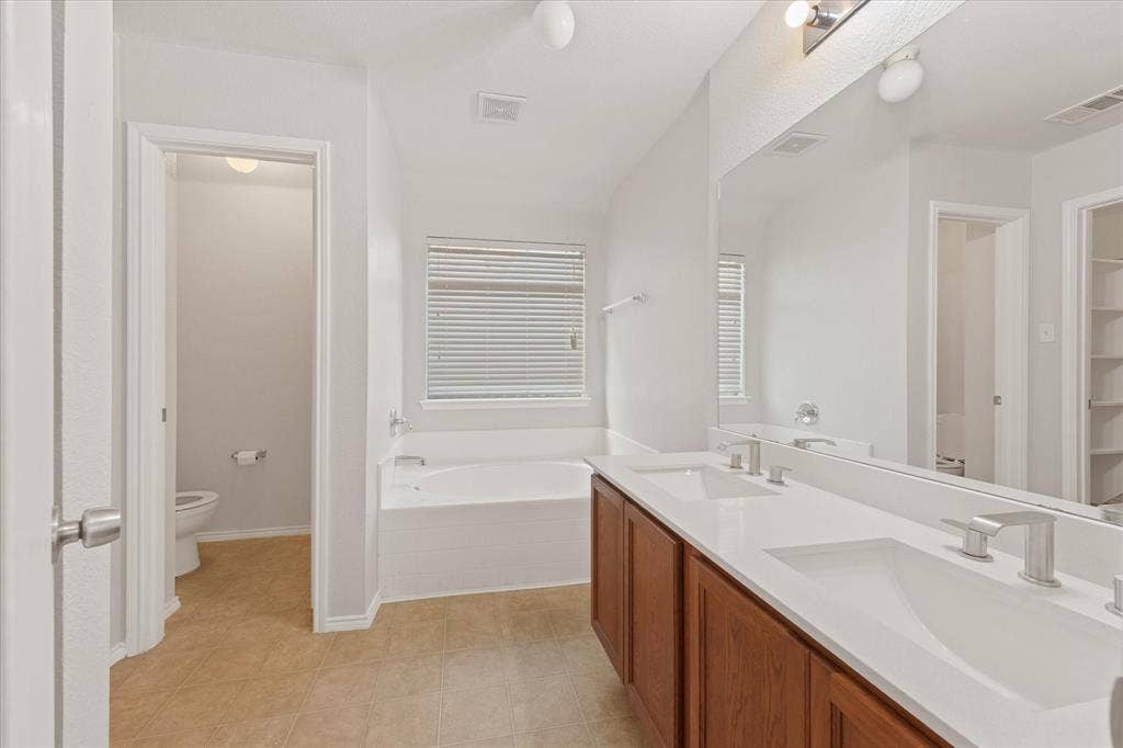 2004 Athabasca Falls Drive, Anna, TX 75409 Double vanity featuring wood-finish cabinetry, quartz countertops, integrated rectangular sinks, and a full-width wall mirror