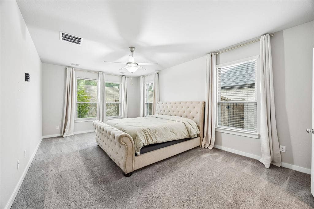 Neutral-toned room featuring four large windows, carpeted flooring, and a ceiling fan with integrated lighting