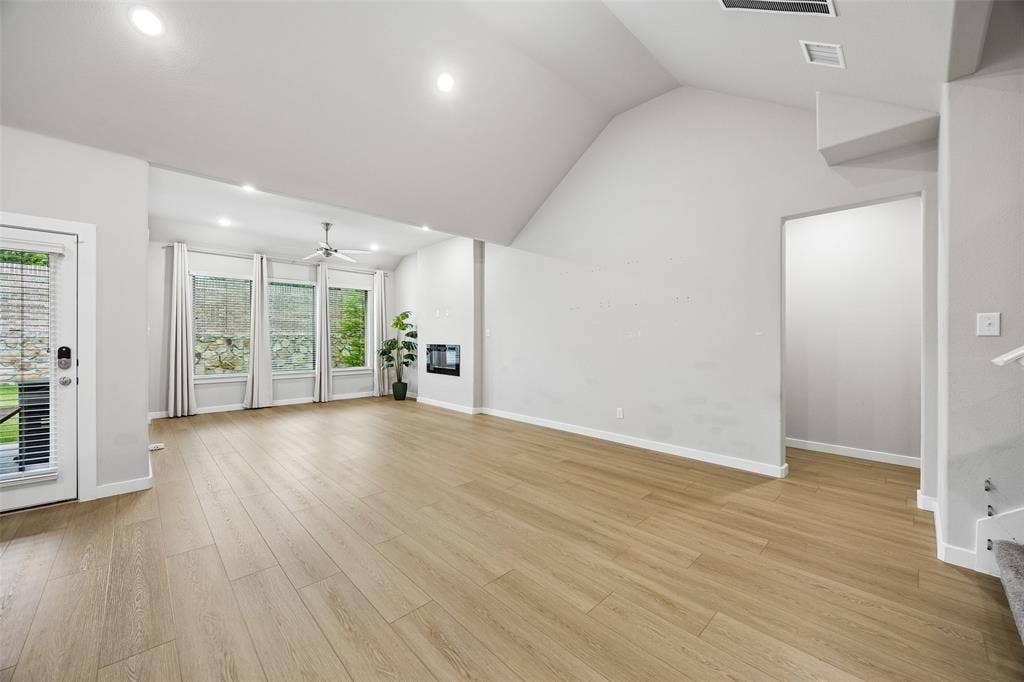 Vaulted ceilings, wood-finish flooring, recessed lighting, wall-mounted fireplace, and large windows