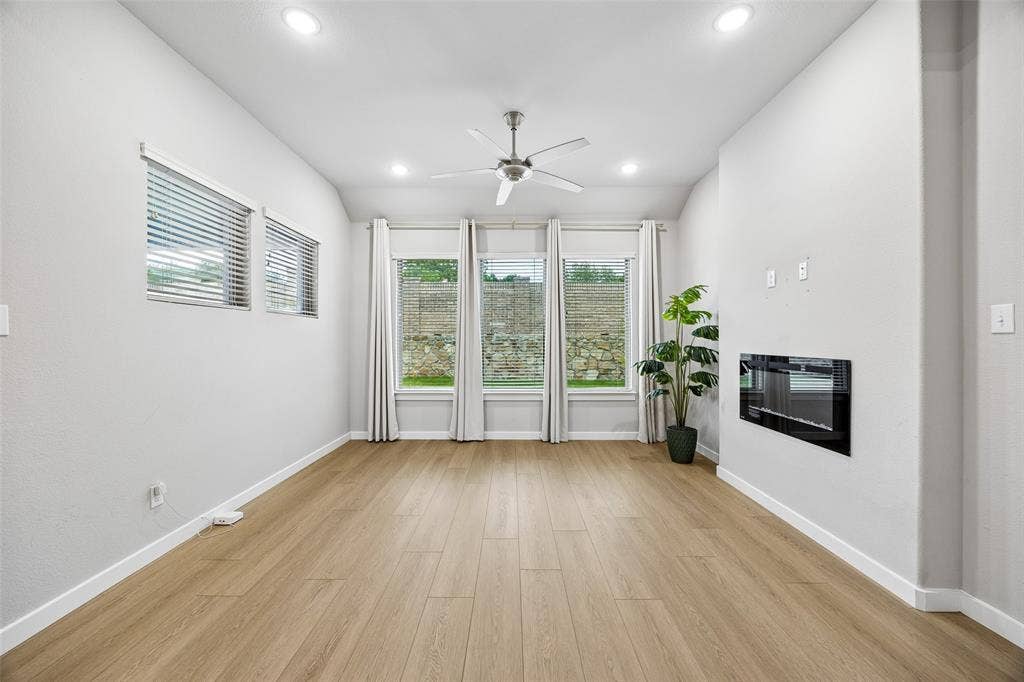 Vaulted ceiling with recessed lighting, wood-finish flooring, triple-pane window array, and wall-mounted electric fireplace