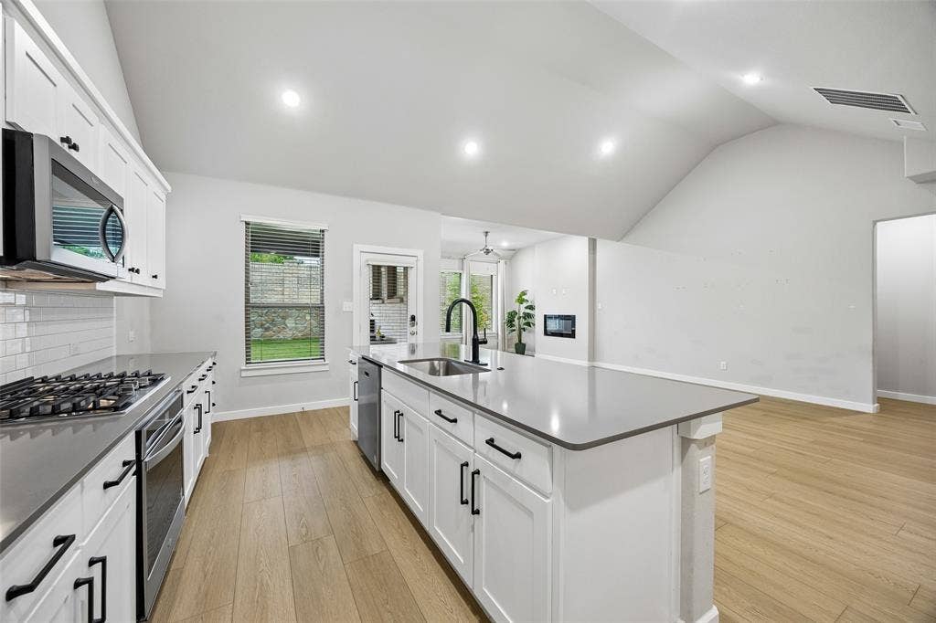 Kitchen featuring a large central island with quartz countertops, white shaker-style cabinetry, matte black hardware, recessed lighting, and wood-finish flooring under a vaulted ceiling