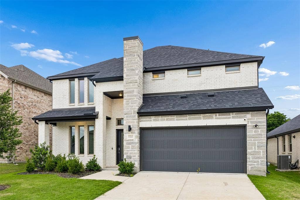 Two-story exterior featuring a white brick and stone facade, a multi-gabled asphalt shingle roof, a two-car garage with a paneled door, and a covered entryway