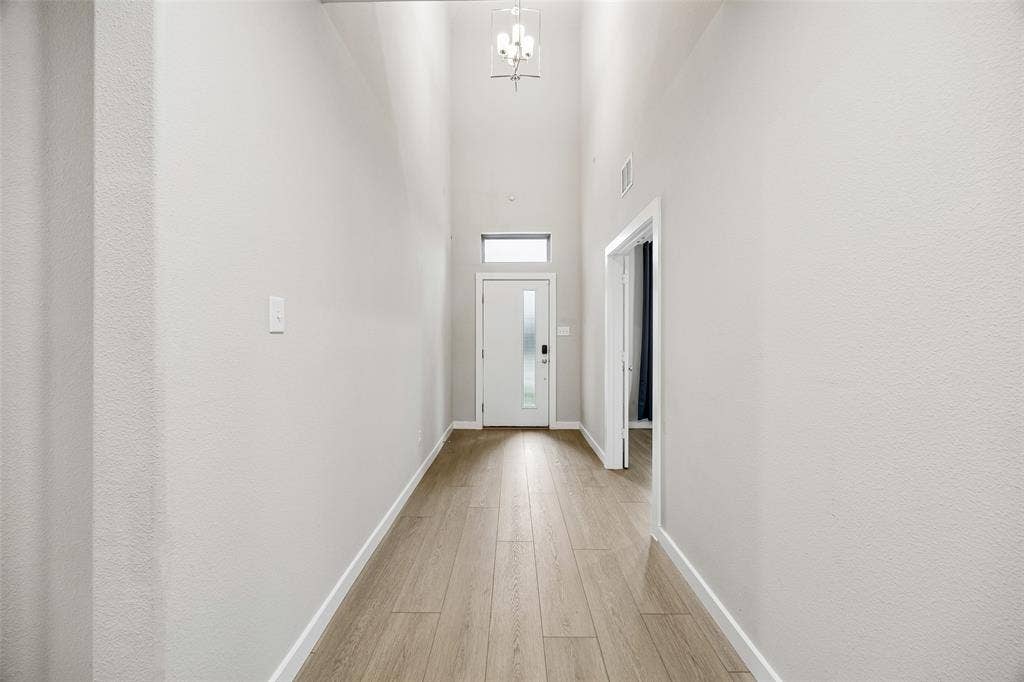 Entryway featuring high ceilings, wood-finish flooring, a metal pendant light fixture, and a glass-paneled entry door with a transom window