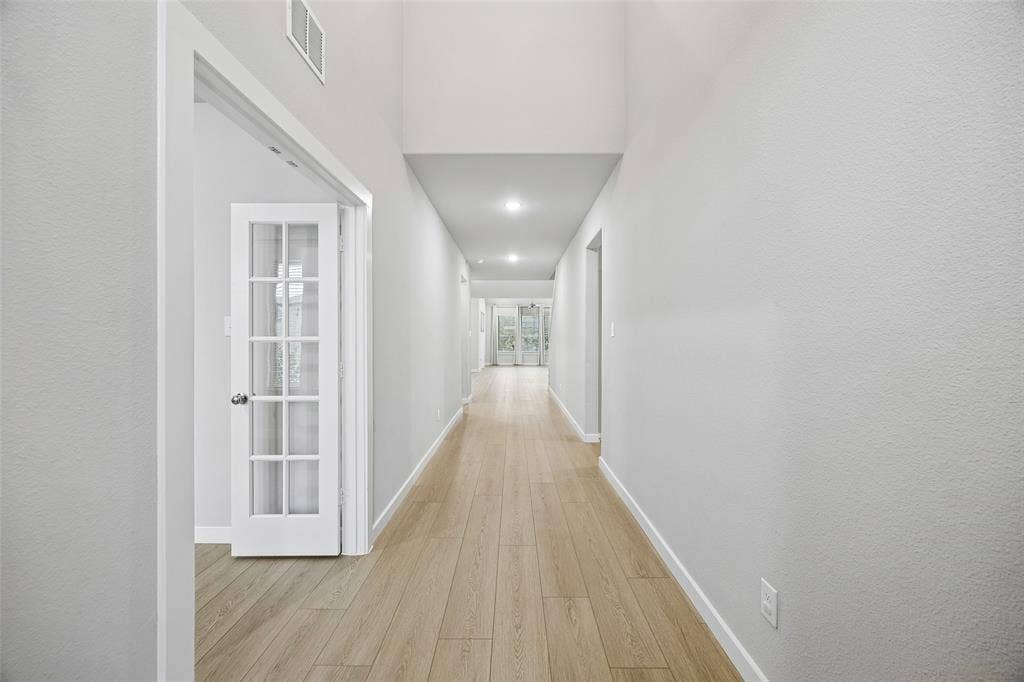 Hallway featuring high ceilings, wood-finish flooring, recessed lighting, and a white French door