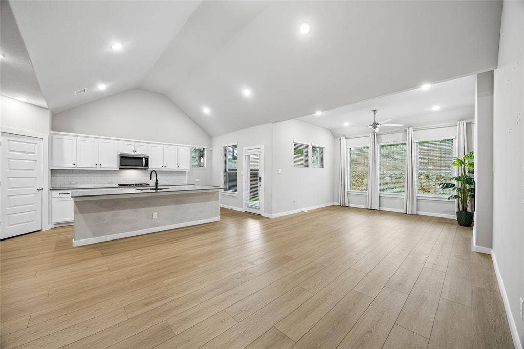 Vaulted ceilings, wood-finish flooring, recessed lighting, kitchen island with a matte black faucet, and large windows with integrated trim