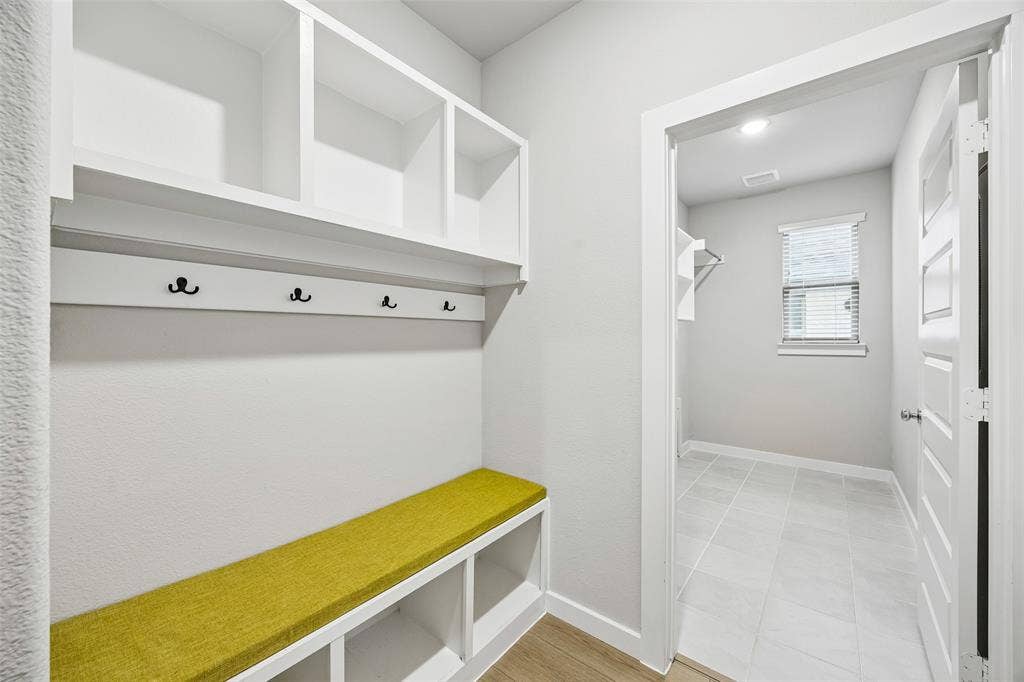 Built-in white storage cabinetry featuring upper cubbies, integrated wall hooks, and a bench with lower open shelving