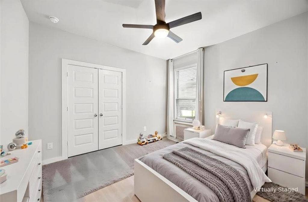 Neutral-toned interior featuring a ceiling fan with integrated lighting, dual-panel closet doors, and a window with neutral-toned wall paint