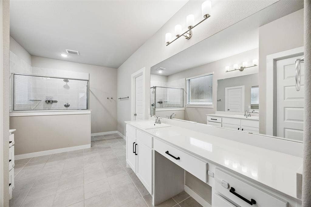 Dual vanity with quartz countertops, white cabinetry with matte black hardware, full-width vanity mirror, walk-in shower with glass enclosure, and ceramic tile flooring
