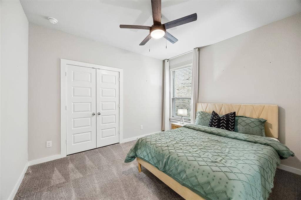 Bedroom featuring neutral wall paint, carpeted flooring, a multi-panel double closet door, and a central ceiling fan with an integrated light fixture