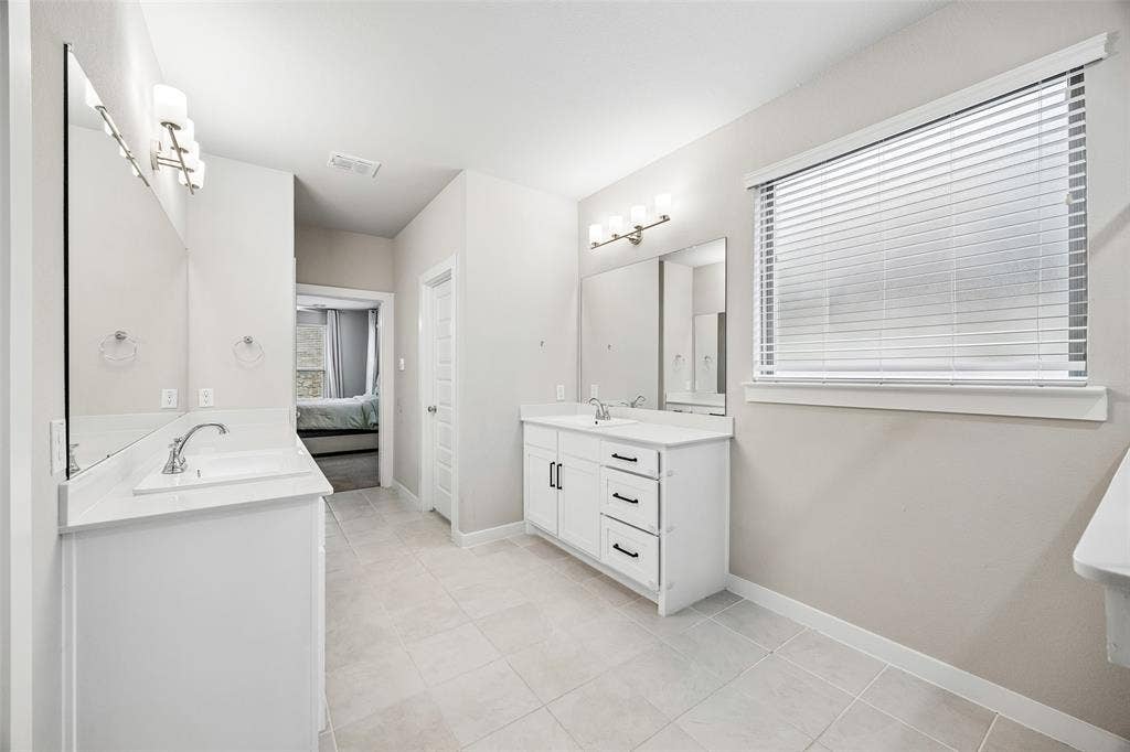Dual vanity area featuring white cabinetry with dark hardware, stone-style countertops, large rectangular wall mirrors, polished chrome fixtures, and ceramic tile flooring
