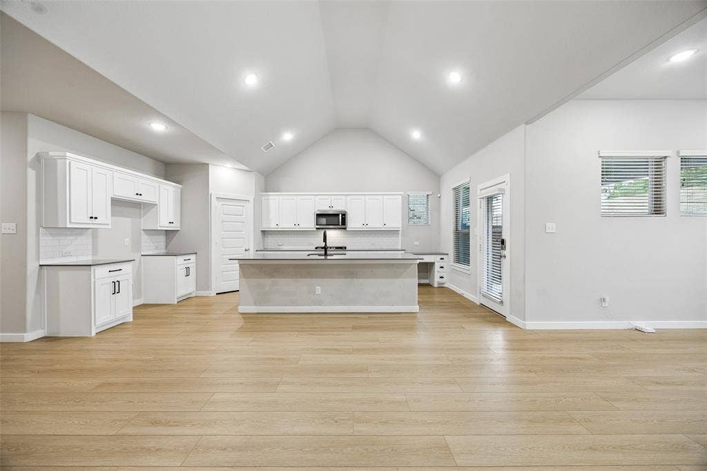 Vaulted ceilings, wood-finish flooring, white cabinetry, a center island, and recessed lighting