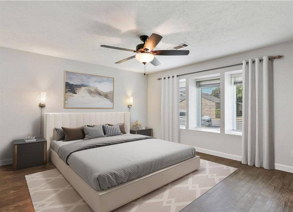 9712 Summerhill Lane, Dallas, TX 75238 Bedroom featuring wood-finish flooring, three windows with natural light, a ceiling fan with integrated light fixture, and two wall-mounted sconces