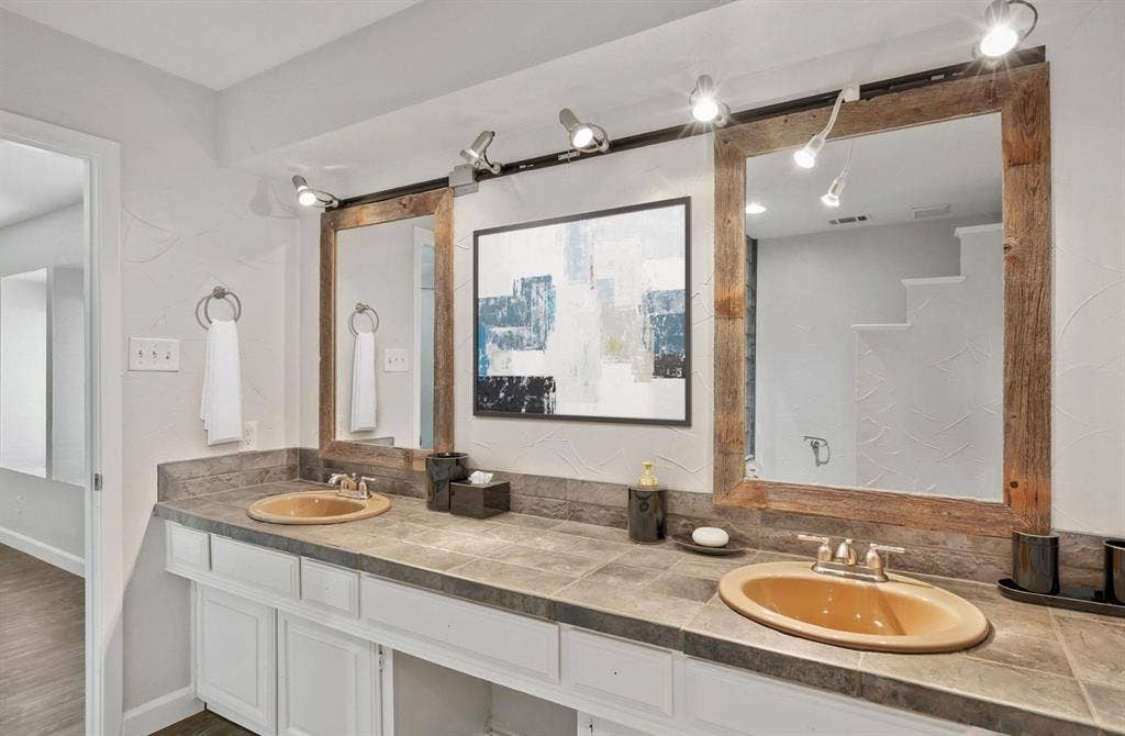 9712 Summerhill Lane, Dallas, TX 75238 Dual-sink vanity featuring tile countertops, white cabinetry, integrated wood-framed mirrors, and track lighting