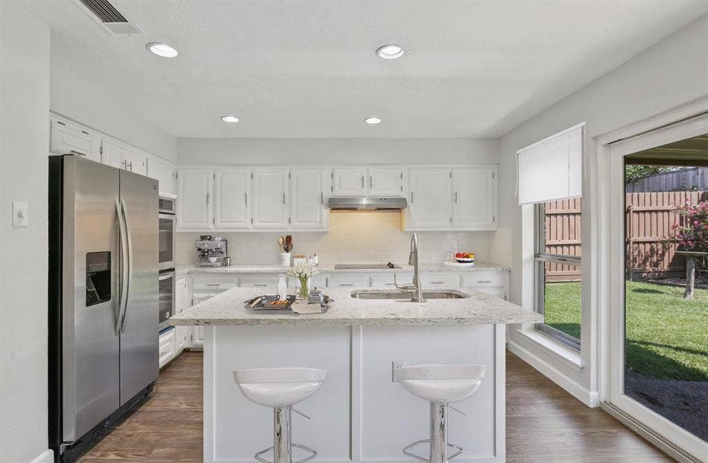 9712 Summerhill Lane, Dallas, TX 75238 Kitchen featuring a center island with a stone countertop, white shaker-style cabinetry, stainless steel appliances, recessed lighting, and wood-finish flooring