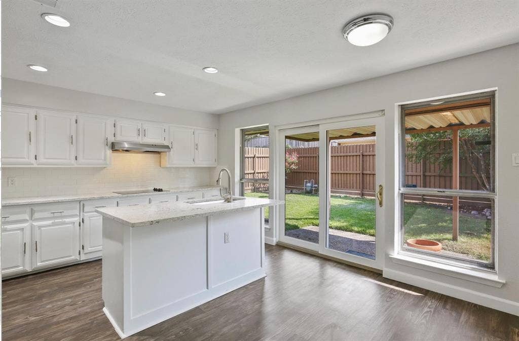 9712 Summerhill Lane, Dallas, TX 75238 Kitchen featuring white cabinetry, stone-surface countertops, central island, wood-finish flooring, and sliding glass door access to a fenced rear yard