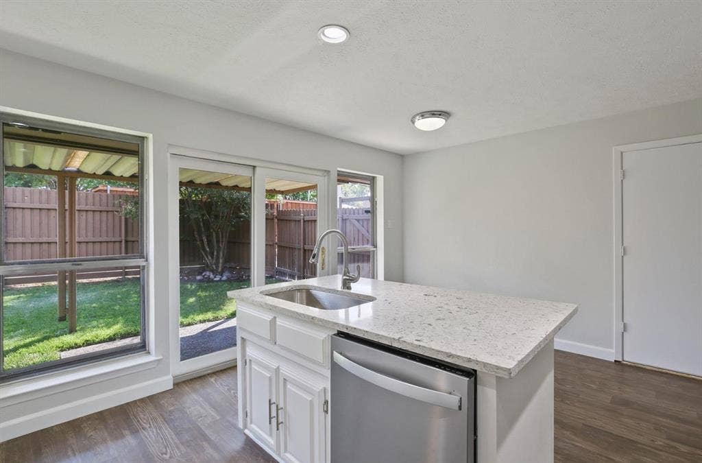 9712 Summerhill Lane, Dallas, TX 75238 Kitchen island featuring a stone-composite countertop, stainless steel undermount sink with a gooseneck faucet, built-in stainless steel dishwasher, white cabinetry, and wood-finish flooring