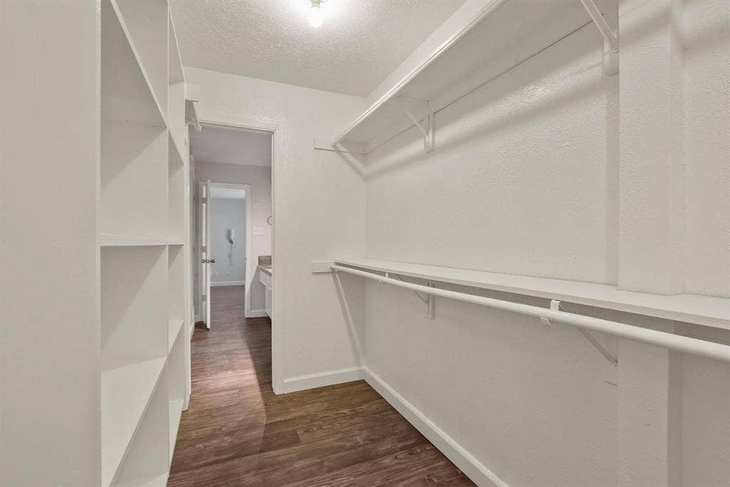 9712 Summerhill Lane, Dallas, TX 75238 Walk-in closet featuring built-in vertical shelving, dual-tier hanging rods, and wood-finish flooring
