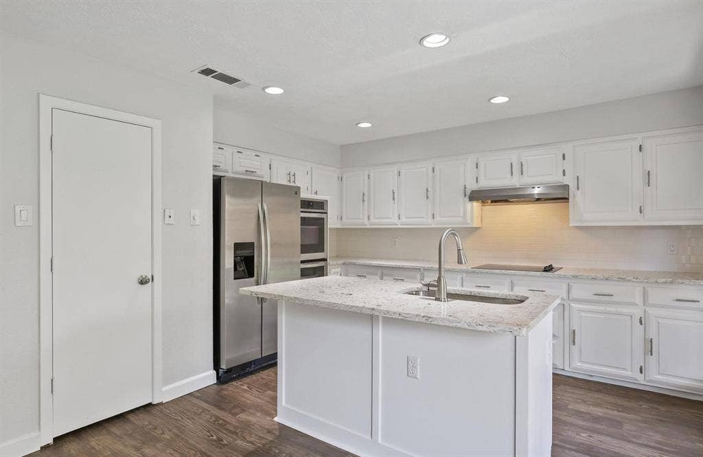 9712 Summerhill Lane, Dallas, TX 75238 Kitchen featuring white cabinetry, stone-surface countertops, central island with an integrated sink, stainless steel appliances, and wood-finish flooring