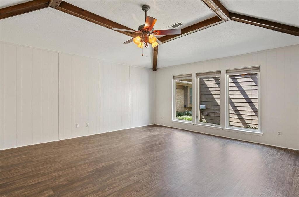 9712 Summerhill Lane, Dallas, TX 75238 Vaulted ceilings featuring exposed wood-finish beams, wood-finish flooring, and a central ceiling fan with integrated lighting, complemented by a trio of windows