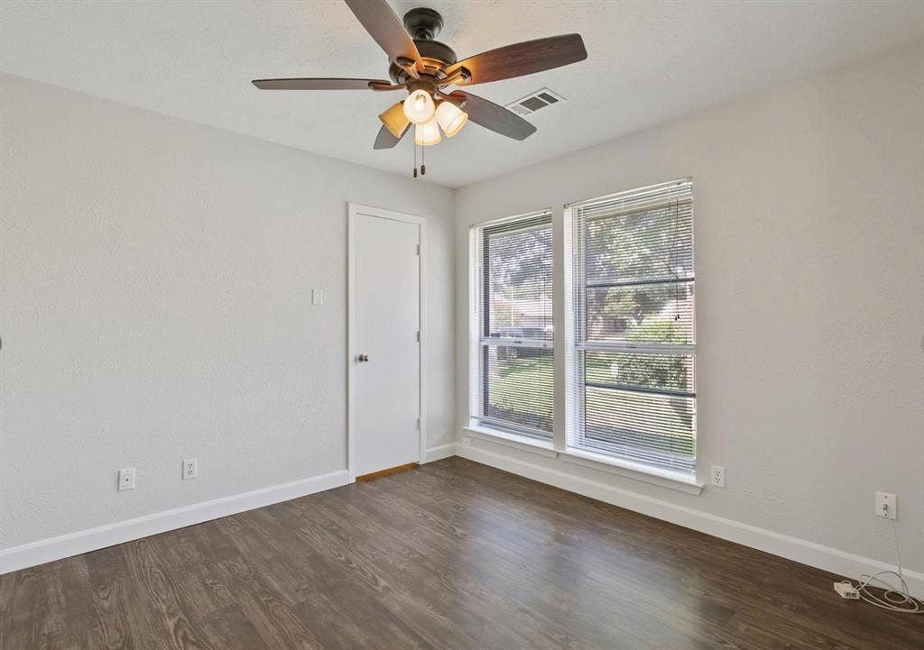 9712 Summerhill Lane, Dallas, TX 75238 Neutral-toned interior room featuring wood-finish flooring, dual windows with integrated blinds, and a multi-blade ceiling fan with a triple-light fixture